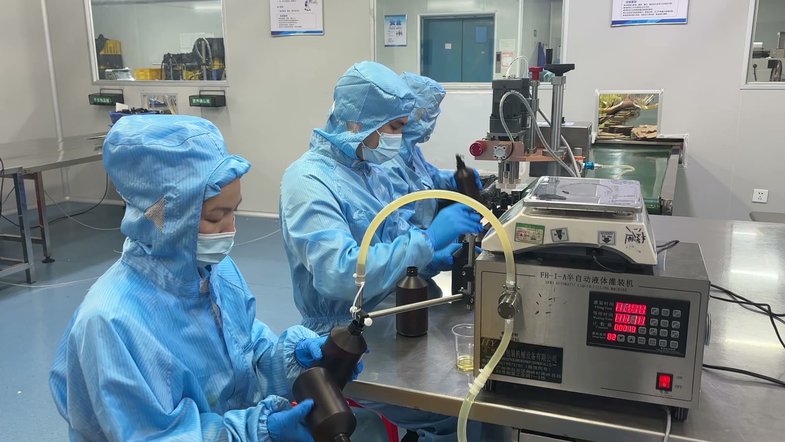 Two operators in clean-room suits filling amber bottles with massage oil